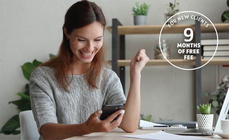 Dekle sedi za pisalno mizo. V eni roki drži pametni telefon, drugo roko ima dvignjeno. Na mizi so listi papirja, pisalo, v ozadju pa so vidne rastline. Na desni strani slike je v krogu napisano besedilo: Za nove stranke 9 mesecev brezplačno.