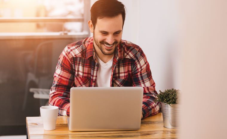 Moški doma sedi za mizo in dela na prenosniku v jutranji svetlobi.