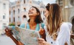 Nasmejani dekleti v mestnem središču z zemljevidom v roki Nasmejani dekleti v mestnem središču z zemljevidom v roki