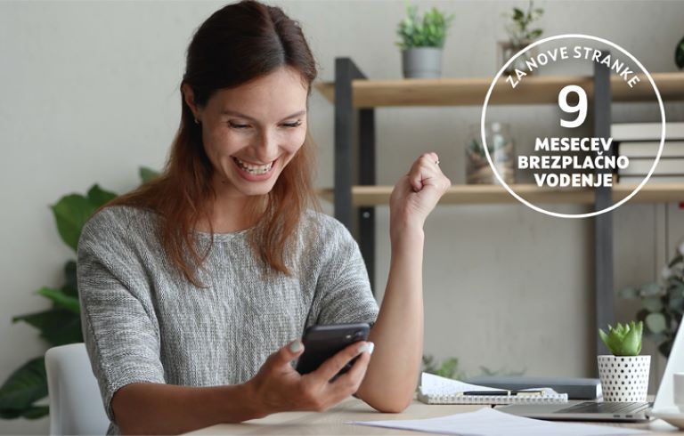 Dekle sedi za pisalno mizo. V eni roki drži pametni telefon, drugo roko ima dvignjeno. Na mizi so listi papirja, pisalo, v ozadju pa so vidne rastline. Na desni strani slike je v krogu napisano besedilo: Za nove stranke 9 mesecev brezplačno.