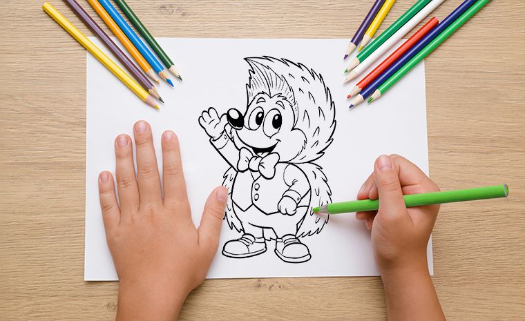 Otrok barva pobarvanko ježka z barvicami na leseni mizi.