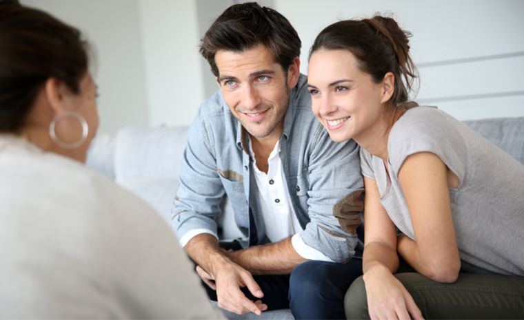 Par sedi na kavču in se pogovarja z osebo, ki sedi nasproti njiju. Oblečeni so v pastelne barve