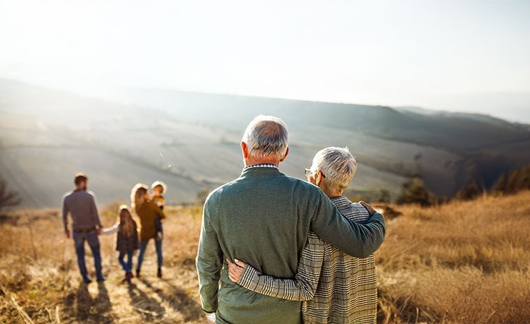 Starejši par opazuje družino pri igri na travnatem pobočju