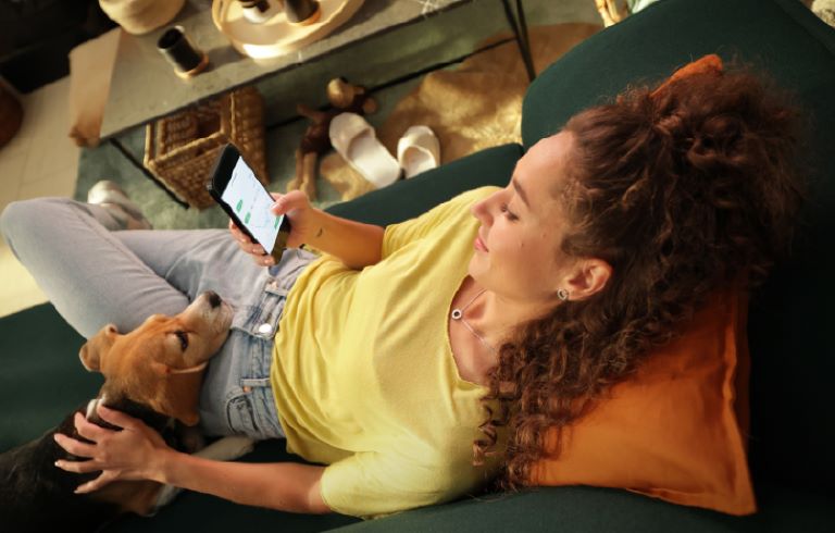 Dekle na kavču z mobilnim telefonom v roki in psom v naročju.