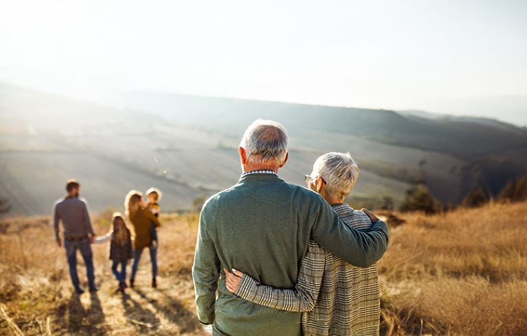 Starejši par opazuje družino pri igri na travnatem pobočju